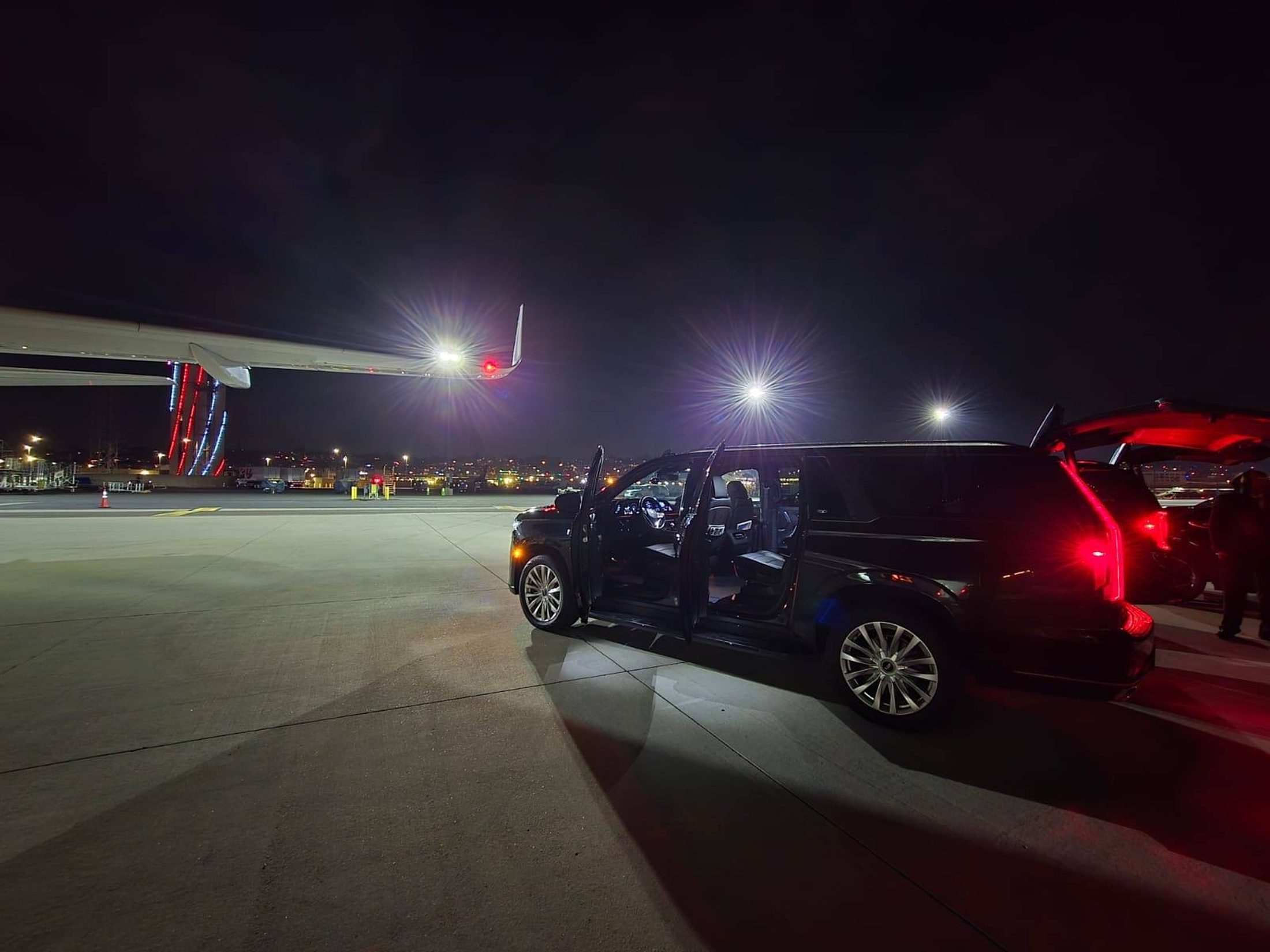 Luxier Cadillac Escalade planeside at night beside a private jet